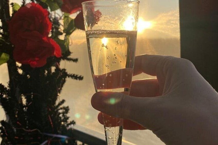Una mano sosteniendo una copa de champán con burbujas, una flor roja y un atardecer de fondo. 3