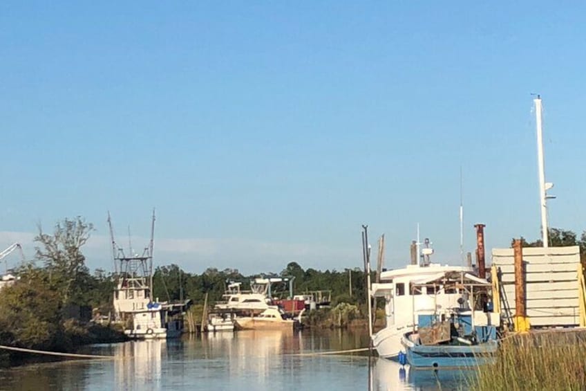 A calm river with boats docked along the shore, surrounded by trees and industrial structures. 5