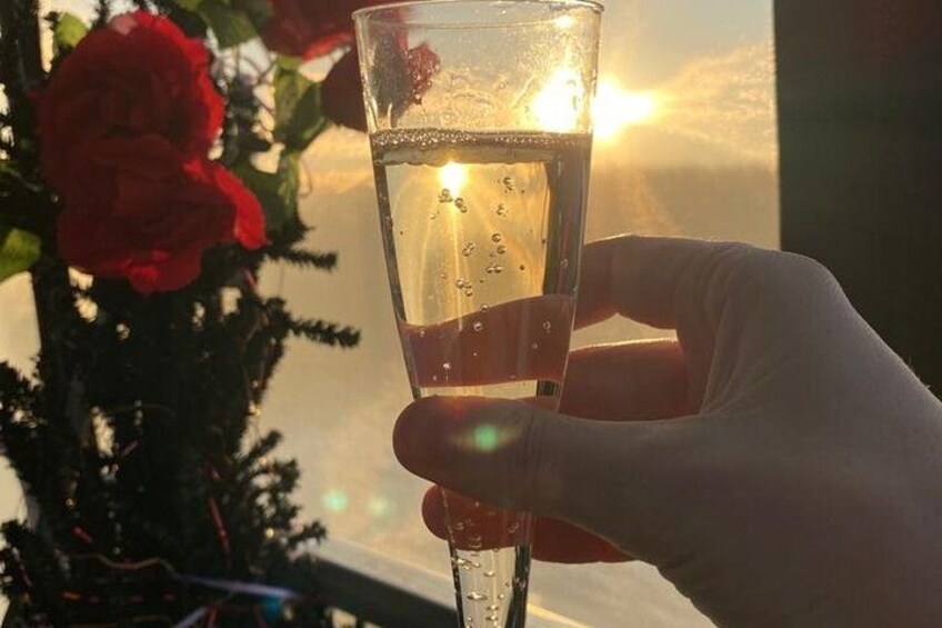 A hand holding a champagne glass with bubbles, a red rose, and a Christmas tree in the background. 3