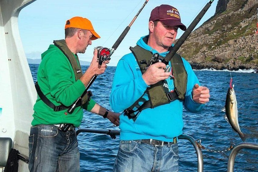 Two people fishing on a boat with a fish in one hand. 4