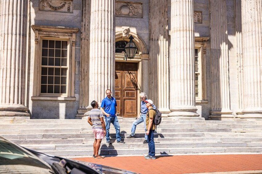 A group of people standing in front of a classical building with large columns and a wooden door. 3