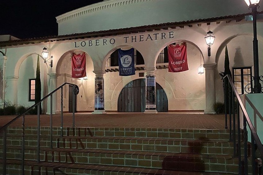 The exterior of the Lobero Theatre with steps leading up to the entrance, arched doorways, and banners hanging above. 2