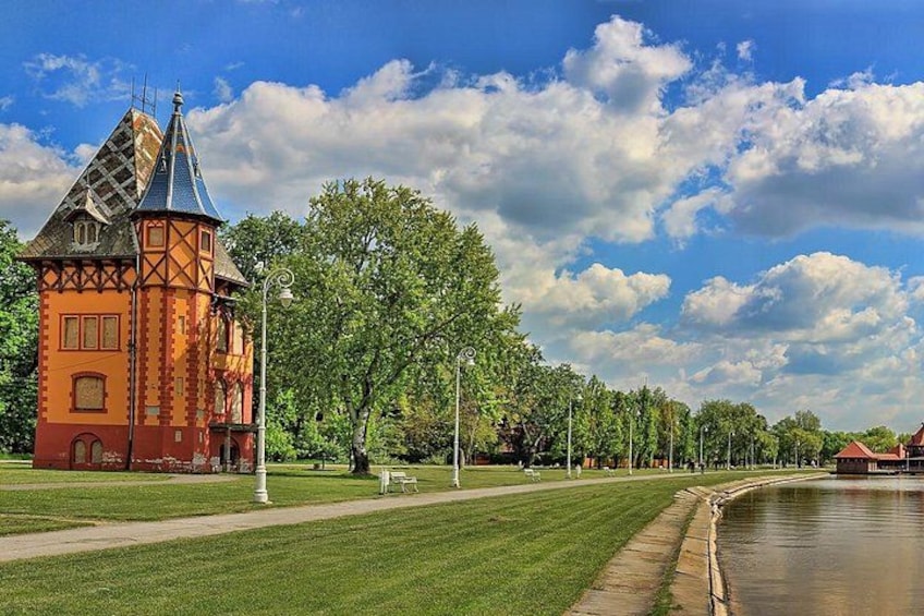 A historic building with a tower, a canal, and a park with trees and a clear sky. 5