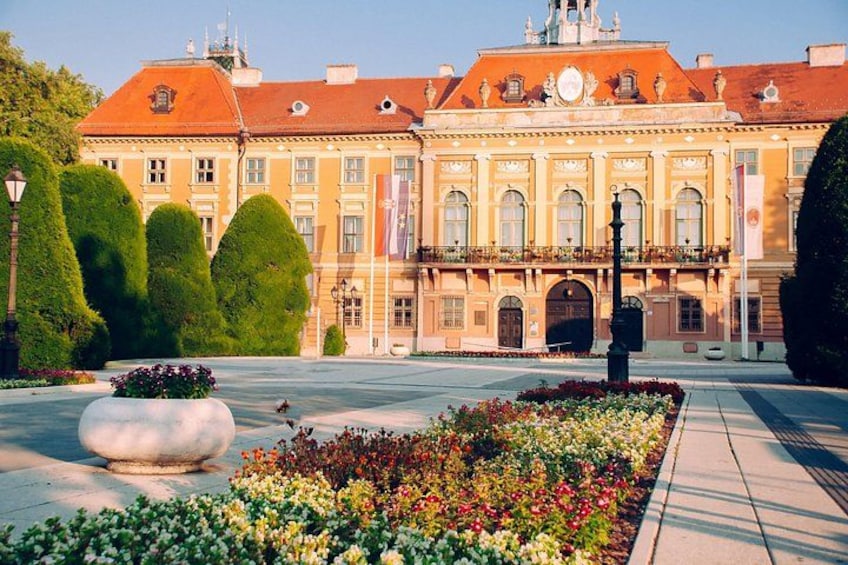 A large, ornate building with a red roof and symmetrical windows, surrounded by well-manicured gardens and a paved courtyard. 3