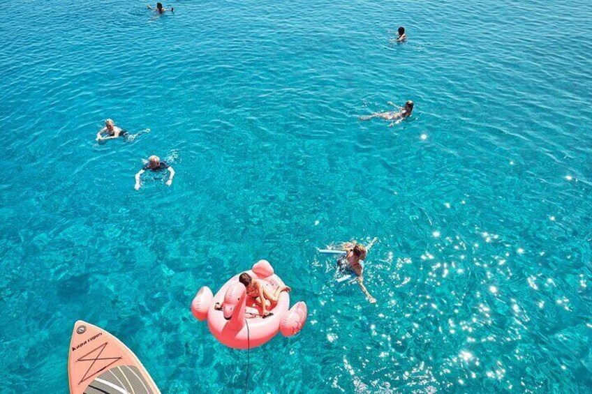 People swimming in a clear blue pool with a pink floatation device. 5