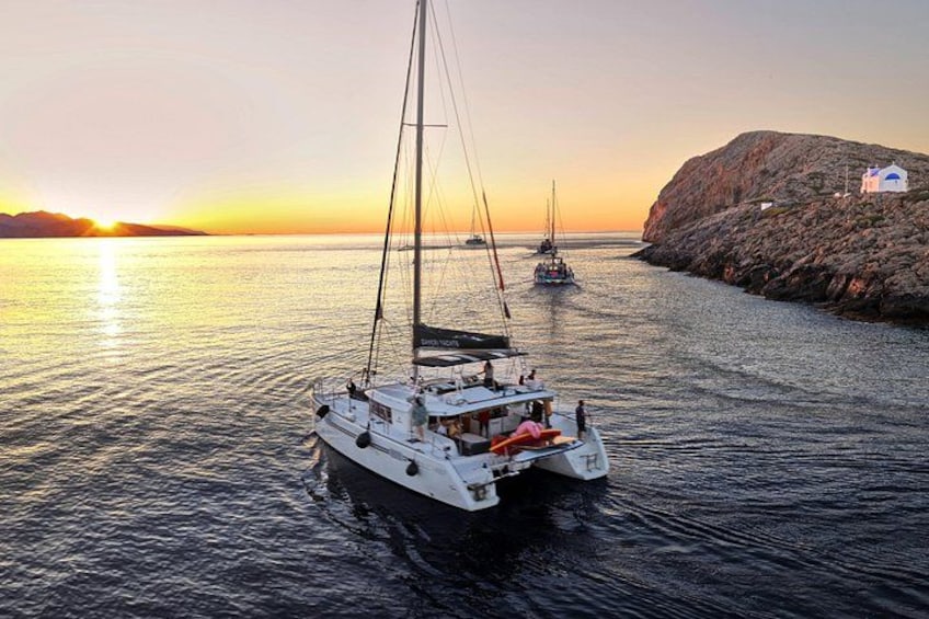 A sailboat on calm waters with a sunset in the background and a rocky outcrop on the right. 2