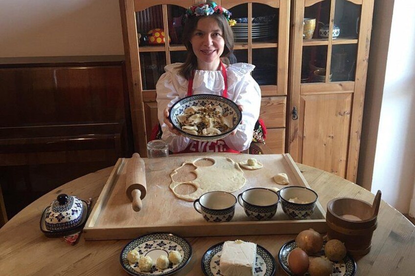 A person in a kitchen holding a plate of food, with a rolling pin, dough, and bowls on the table. 3