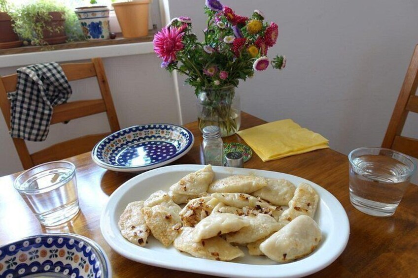 A plate of dumplings on a table with a vase of flowers, a glass of water, and a checkered cloth. 5