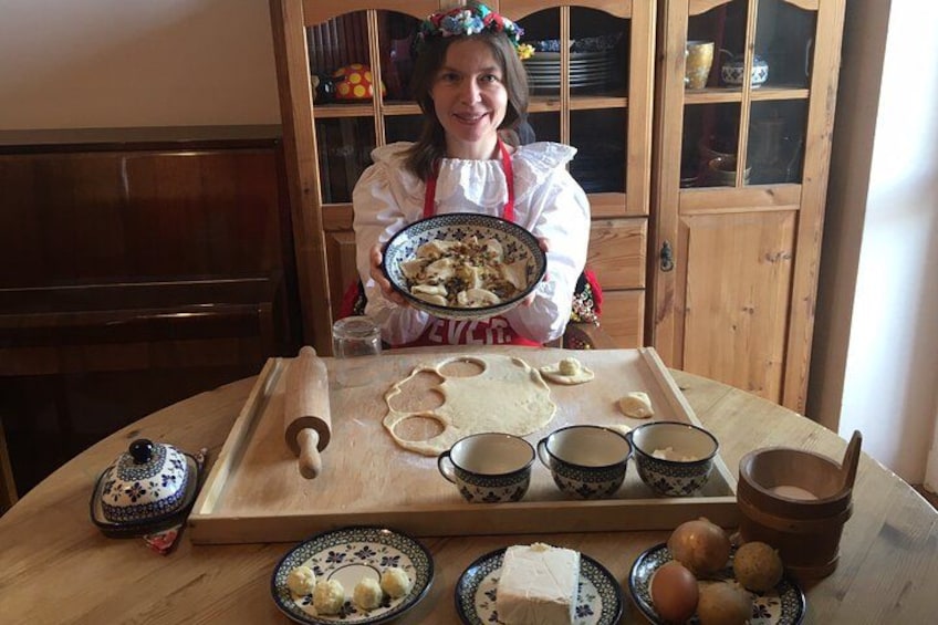 A person holding a plate with food, a rolling pin, dough, and bowls on a wooden table. 2