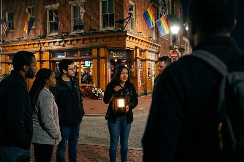 A group of people standing on a street at night, a brick building with flags, and a person holding a lantern. 1