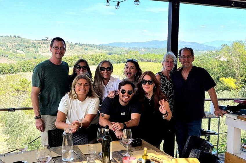 Un grupo de personas sentadas a una mesa con copas y botellas de vino, con vistas a un paisaje pintoresco. 2