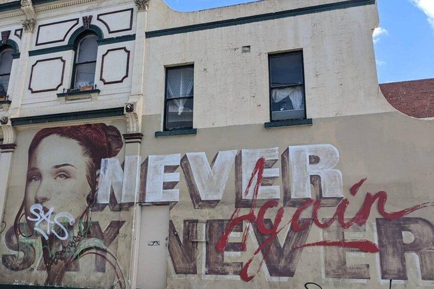 Un edificio con grafitis en su fachada, incluyendo las palabras 'NEVER AGAIN' y un retrato parcial. 5