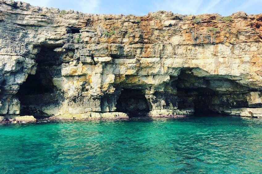 A coastal cliff with a cave entrance and turquoise water. 1