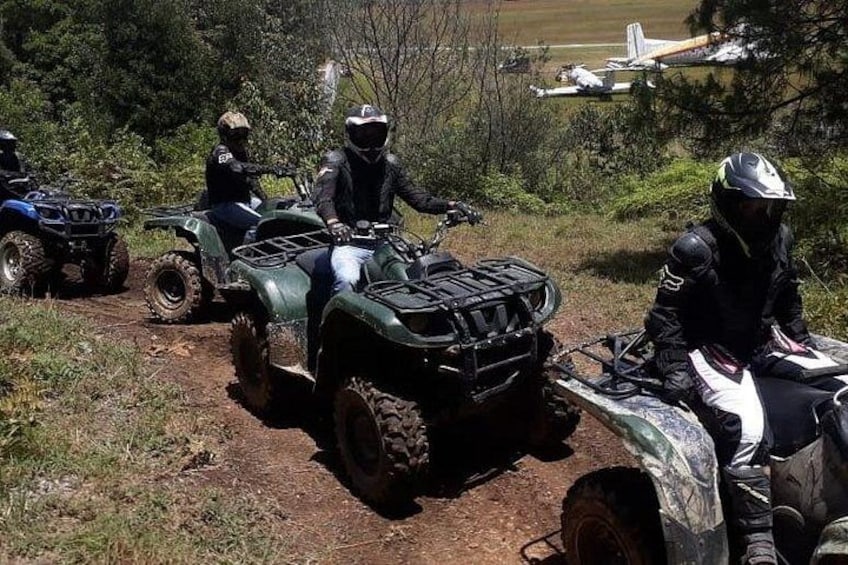 Three off-road vehicles on a dirt path with trees and a distant airplane in the background. 1