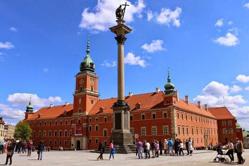 A large red building with a clock tower, a central monument, and people walking around. 5