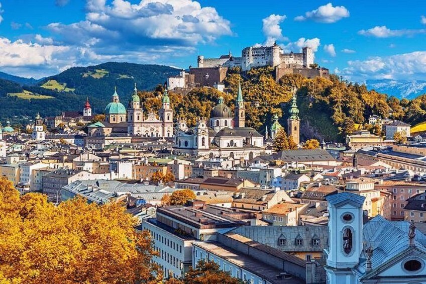 A historic city with a castle on a hill, surrounded by buildings and autumn trees. 3