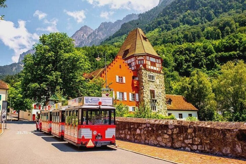 A red and white bus on a road with a mountain backdrop, a traditional building with a tower, and lush greenery. 4