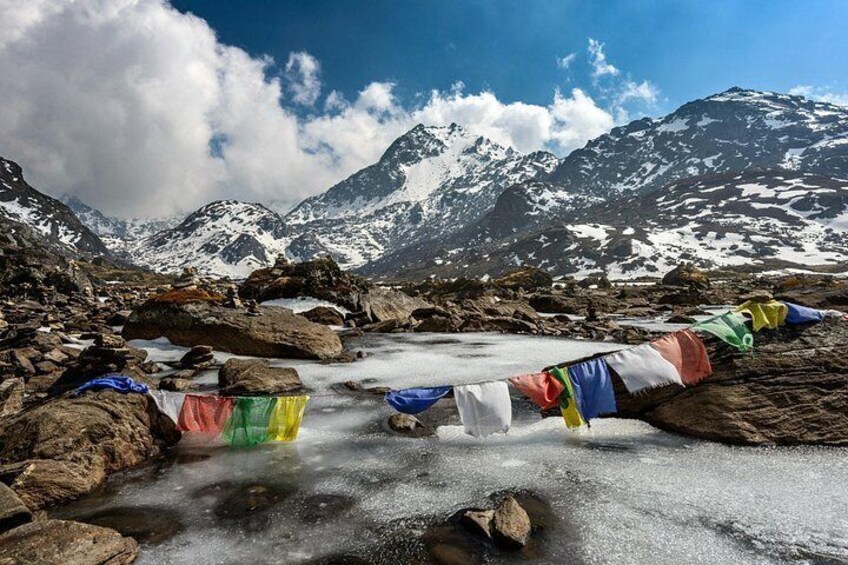 A snowy mountain landscape with a stream and colorful prayer flags. 2
