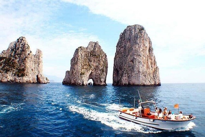 A boat on a calm sea with three large rock formations in the background. 4