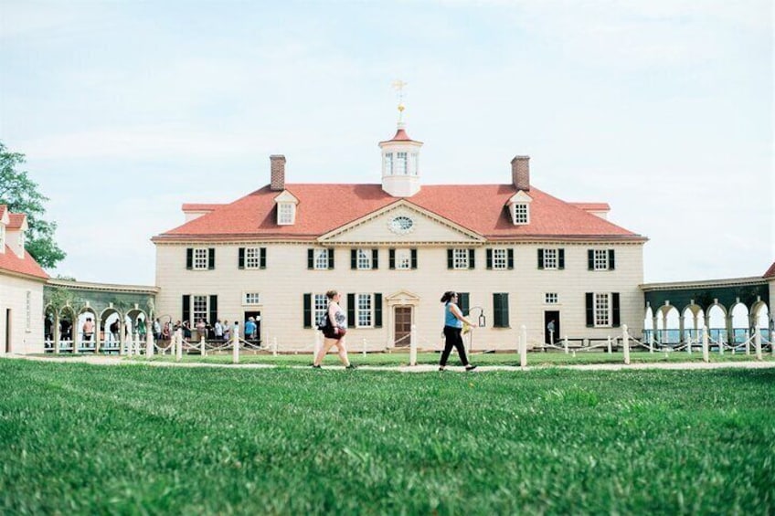 A large historic building with a red roof and white walls, surrounded by a well-maintained lawn and a fence. 1
