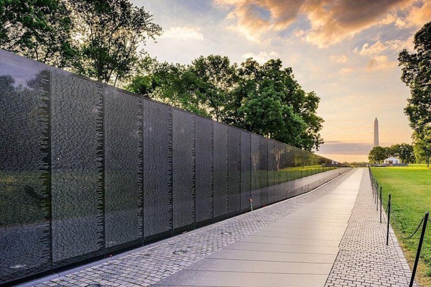 A long memorial wall with engraved names, a paved walkway, and a distant monument. 5