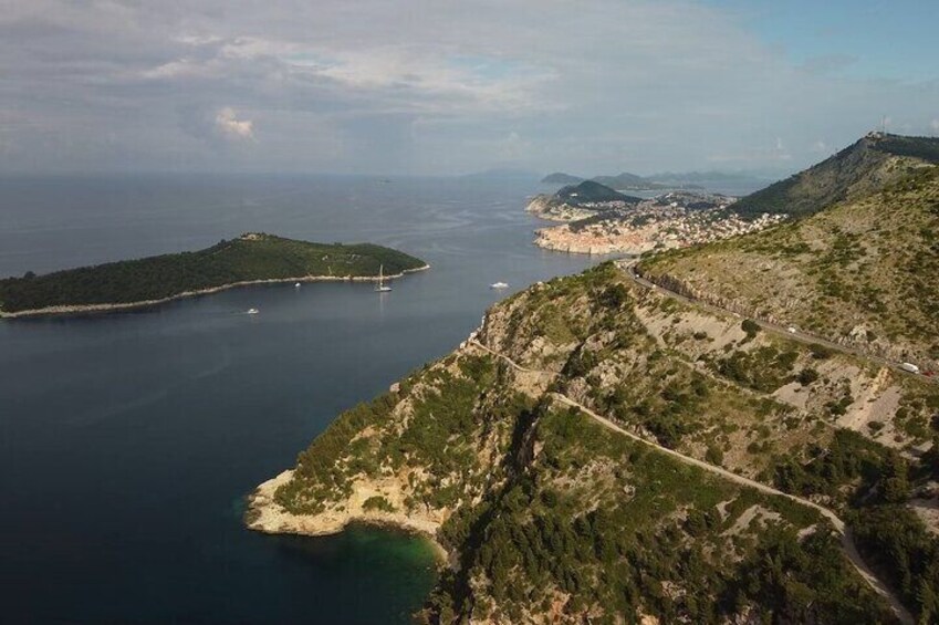 Un paisaje costero con un camino sinuoso, una pequeña isla y un pueblo lejano. 4