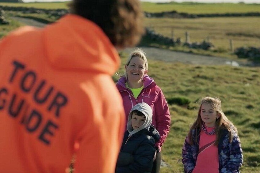 Un guide touristique, vêtu d’une veste orange, accompagne un groupe de personnes dans un champ herbeux. 2