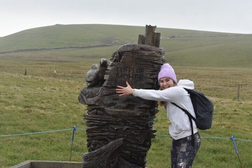 Une personne se tient à côté d’un monument de pierre orné d’inscriptions, entouré d’un champ herbeux et avec des collines en arrière-plan. 4