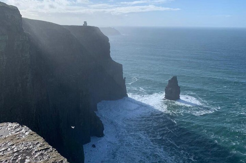 Un acantilado costero con una formación rocosa en el mar, cielo despejado y horizonte distante. 4