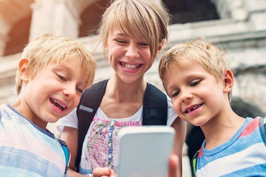 Drie kinderen met een smartphone, een rugzak en een gebouw op de achtergrond. 2