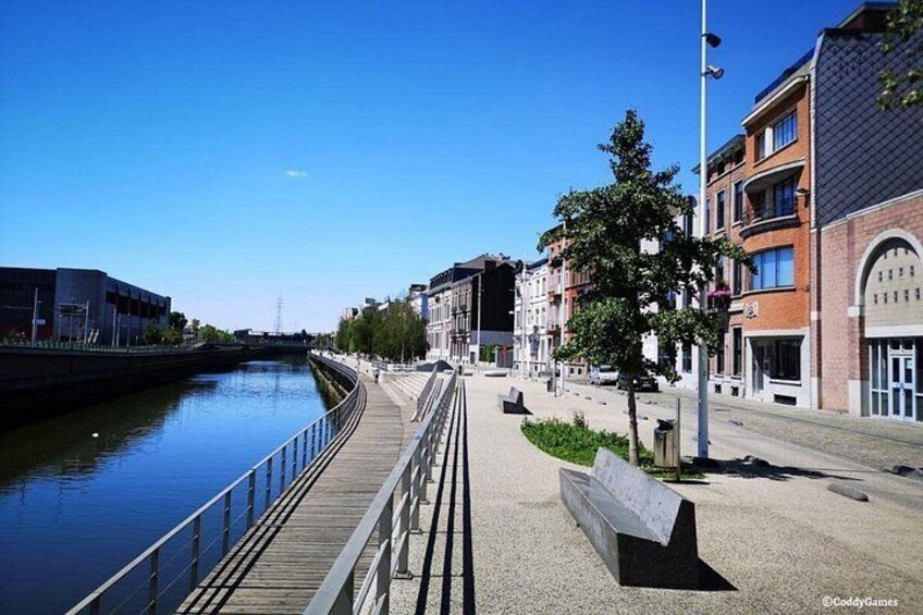 Een wandelpad langs de rivier met een bankje, gebouwen en een heldere lucht. 4