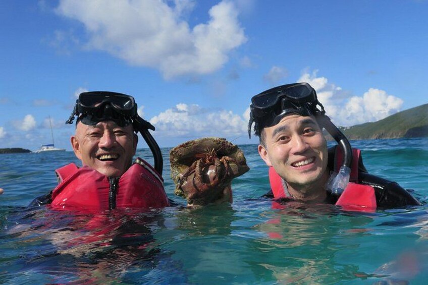 Två personer som snorklar i klart, blått vatten, med en båt och en avlägsen ö i bakgrunden. 5