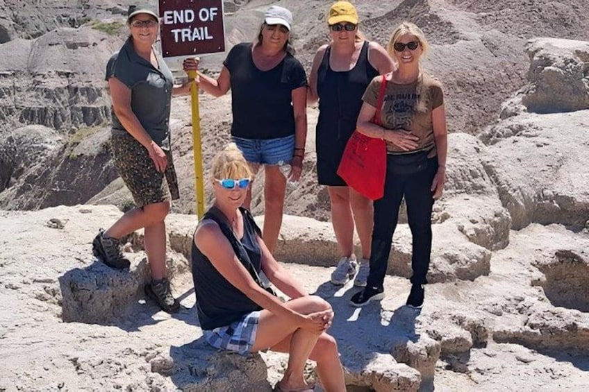 A group of people standing on a rocky trail with a sign that reads 'END OF TRAIL'. 5
