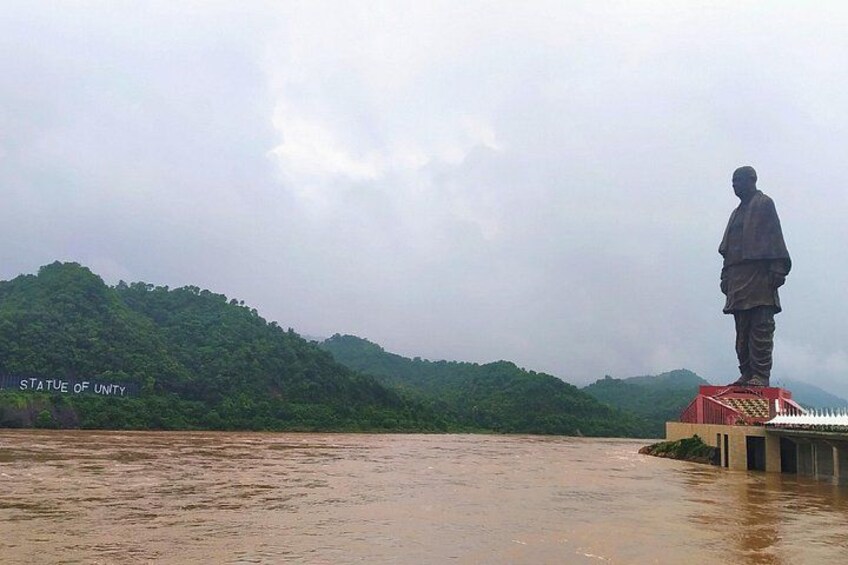 A statue of a man on a platform by a river with a forested hill in the background. 4