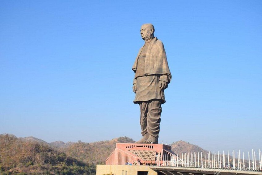 A large statue of a man standing on a platform with a clear sky and mountains in the background. 3