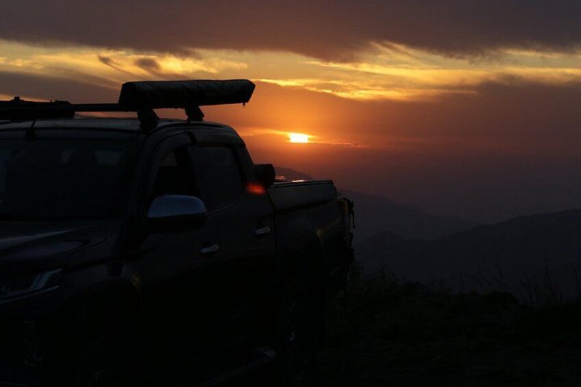 A vehicle parked on a hill with a sunset in the background. 1