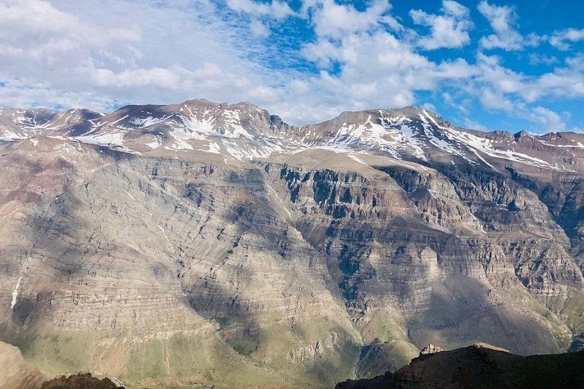 A mountain range with snow-capped peaks and layered rock formations. 5