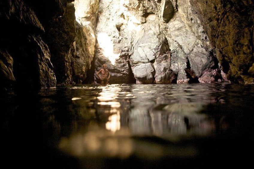 A cave with water reflecting light, rocky walls, and a person standing in the water. 3