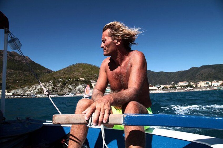 A man on a boat with a mountainous coastline in the background. 2