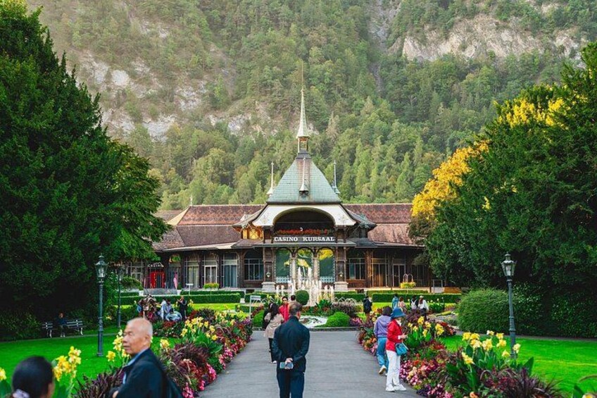 Un bâtiment de casino doté d’un toit végétalisé et d’une flèche, entouré d’un jardin bien entretenu où poussent différentes espèces de fleurs et d’arbres. 3