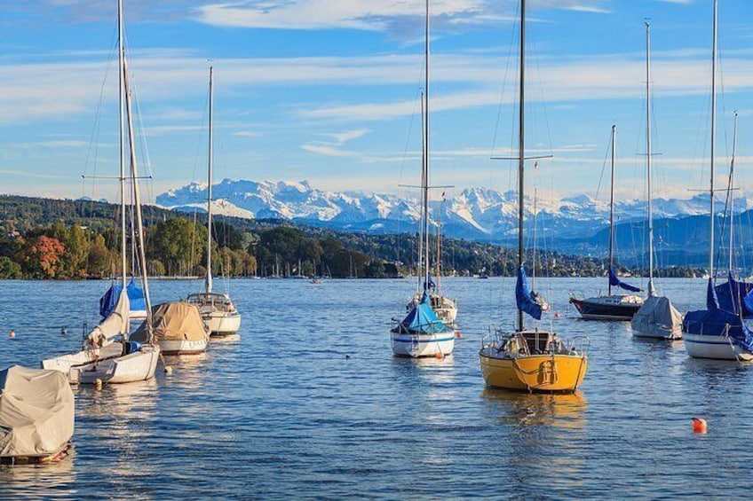 En stilla sjö med segelbåtar som ligger ankrade, berg i bakgrunden och en klar himmel. 1