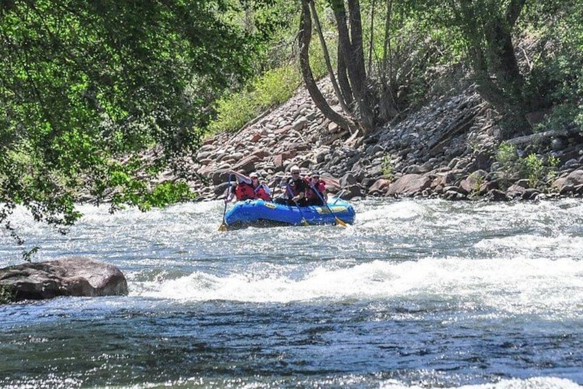 Una balsa azul con dos personas navegando un río rodeado de árboles y rocas. 3