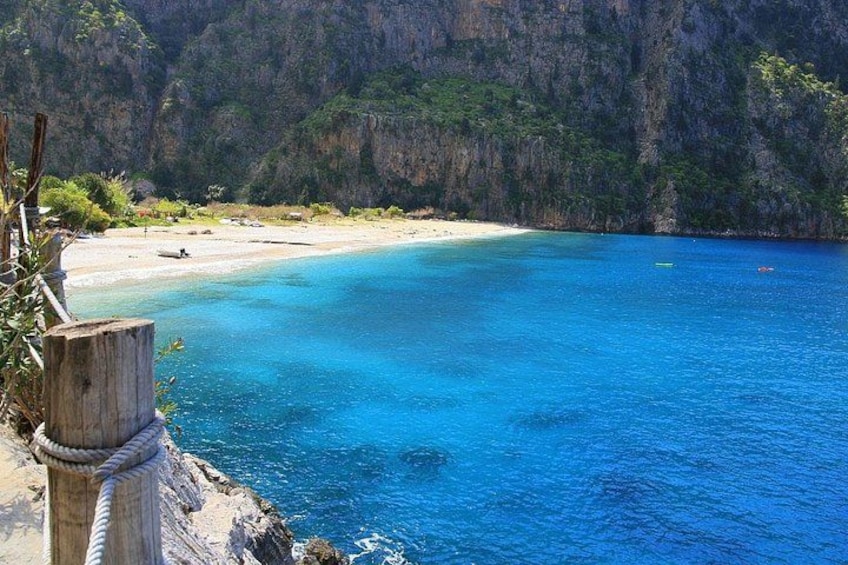 A coastal landscape with clear blue waters, a sandy beach, and a rocky cliff. 3