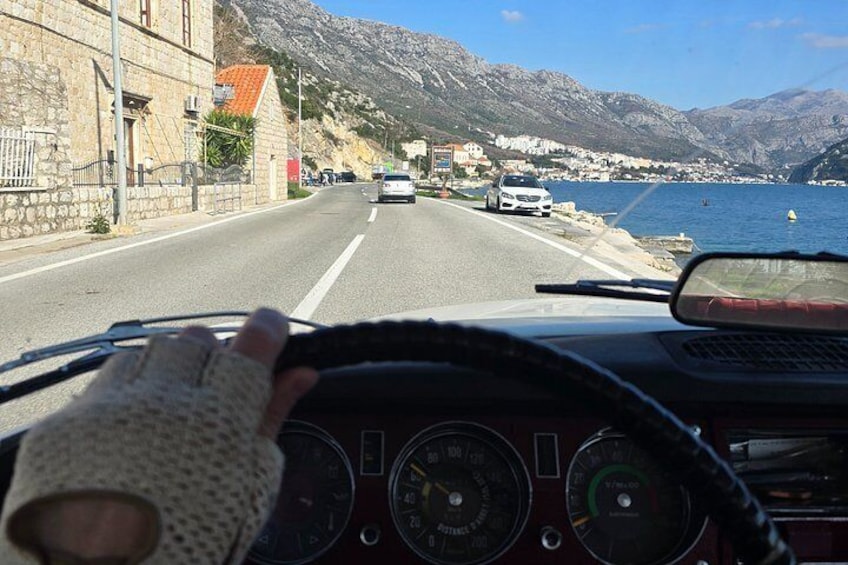 Een voertuig rijdt over een kustweg, met bergen op de achtergrond. 2