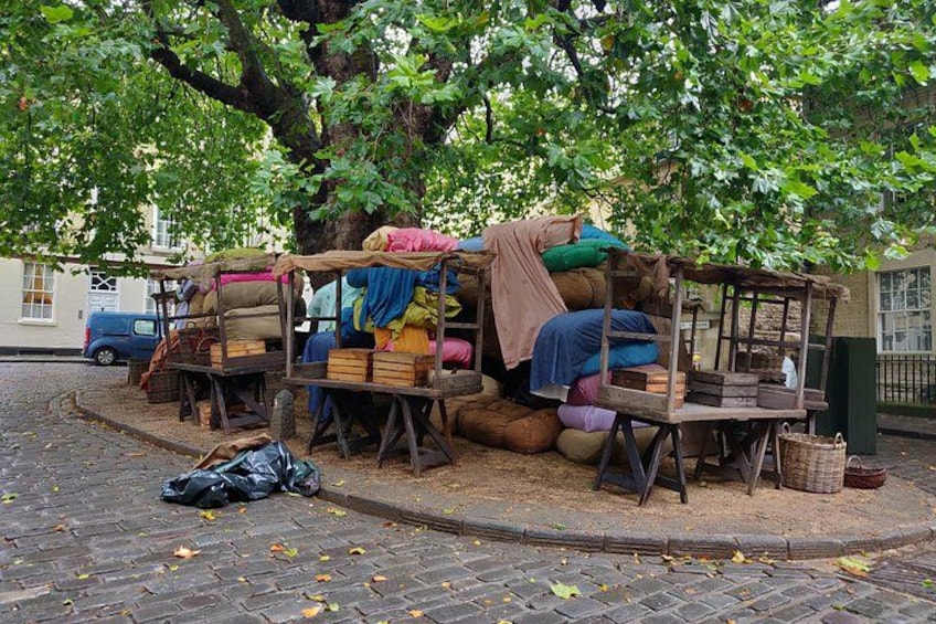 Outdoor furniture under a tree, a blue car, and a brick pavement. 4
