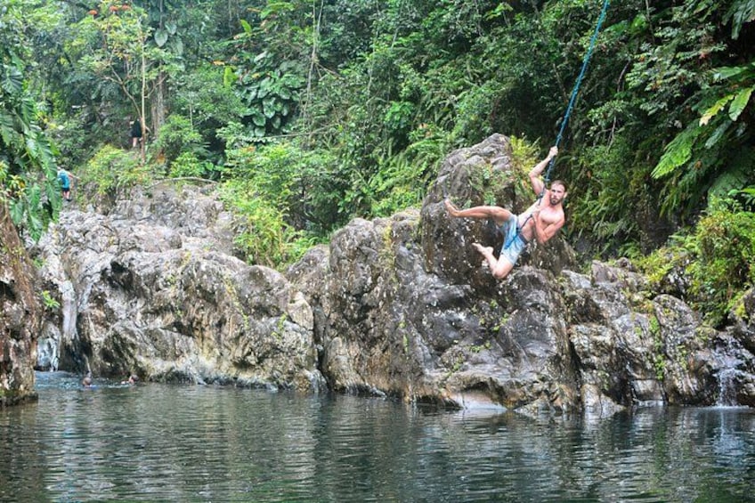 A person swinging on a rope over a river surrounded by rocks and greenery. 2