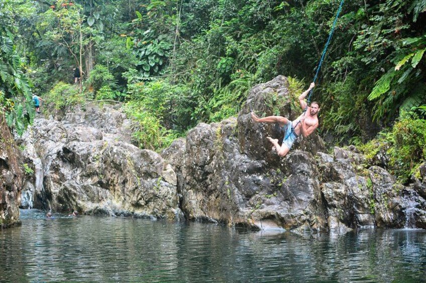 A person swinging on a rope over a river with rocks and greenery in the background. 4