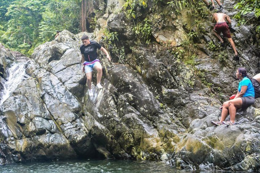 People climbing and sitting on rocks near a waterfall in a forested area. 3