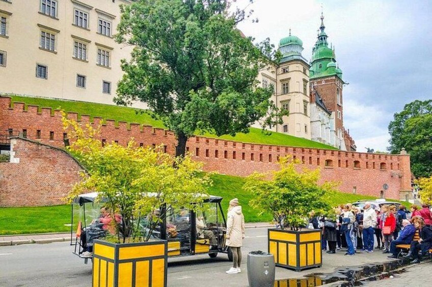A historic building with a green dome, a brick wall, and a paved area with yellow planters and a parked vehicle. 2