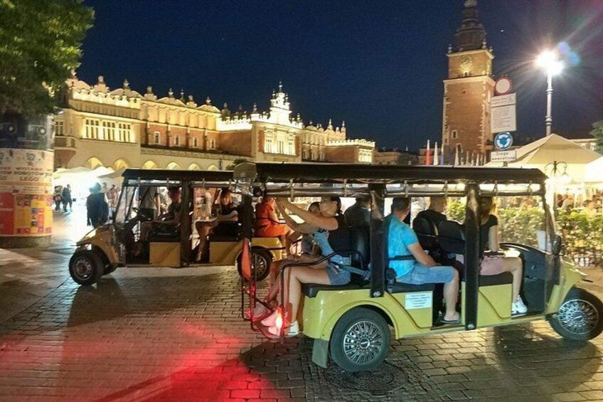 A yellow tram with passengers, a clock tower, and a building with arches in the background. 3